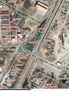 A satellite map showing a road intersection labeled as Old Holman Rd and Main St. Parcel numbers are marked in red across various properties. An empty lot and a neighboring area with assorted items are visible on the right side of the map.