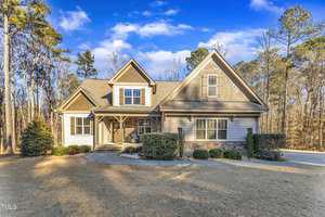 A suburban house with a gable roof, stone and siding exterior, and a small front porch. It is surrounded by a neatly maintained lawn and trees. The sky is clear and sunny.