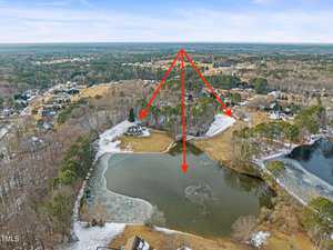 Aerial view of a snowy landscape featuring a partially frozen pond surrounded by trees. Red arrows point from the pond to various locations, including a house and wooded areas. Residential neighborhoods are visible in the background under a blue sky.