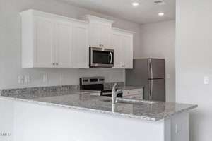 Modern kitchen with white cabinets, granite countertops, and a stainless steel sink. Features a stainless steel refrigerator, microwave, and electric stove. The space has a neutral color scheme and recessed lighting, with a view of the kitchen island.