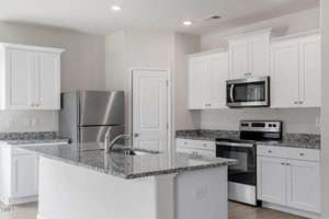 Modern kitchen with white cabinets, stainless steel appliances, and a granite countertop island. There is a refrigerator, oven with a stovetop, and a microwave. The room is well-lit with ceiling lights.