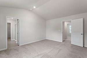 Empty room with light beige carpet, white walls, and a vaulted ceiling. Two open doorways lead to a closet and another room. A third, partially open door is on the right. Recessed lighting is visible on the ceiling.