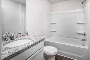 A bathroom with a white bathtub and shower combination, a white toilet, and a vanity with a granite countertop and sink. The walls are white, and the floor is covered with wood-patterned flooring.