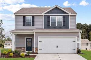 The two-story house at 818 Rhino Bend boasts a gray facade and a white garage door with a charming covered front porch. In Oxford, its landscaped shrubbery graces the front yard, accompanied by a driveway leading to the garage, all set against neighboring houses and a wooded area.