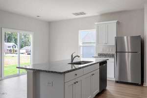 Modern kitchen with white cabinets and stainless steel appliances. Includes a center island with a granite countertop and built-in sink. Light wood flooring and large sliding glass doors open to a grassy yard. Natural light fills the space.