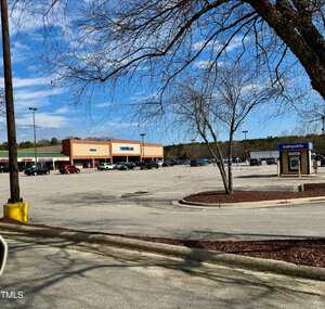 A nearly empty parking lot is in front of a grocery store named "Food Lion." The lot has some parked cars and a Cashpoints ATM on the right. Bare trees and a clear sky are visible in the background.
