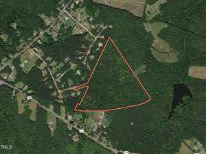 Aerial view of a rural area in Henderson with a red outline marking a triangular piece of land near Taylor Farm Lane. The landscape features houses, roads, dense green forest, and a small body of water on the right.