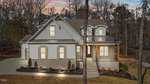 A charming two-story house at 1105 Springdale Drive, with a gray exterior, large windows, and a covered porch, sits amidst Wake Forest's wooded beauty. The driveway gently leads to the front steps, bordered by small shrubs at the base.