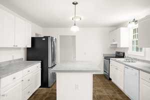 A modern kitchen with white cabinets, a central island, and stainless steel appliances including a refrigerator, oven, and dishwasher. The floor is tiled in brown, and there is overhead lighting.