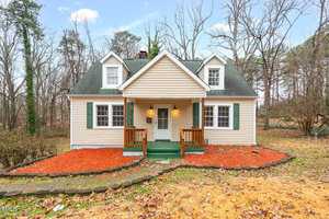 A small, beige house at 673 Beck Avenue in Henderson, featuring a green roof and shutters. It boasts a front porch with wooden railings and a white door. The lawn, blanketed with fallen leaves, is framed by bare trees under a partly cloudy sky.