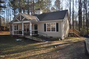 Nestled at 146 Oak Forest Drive, this charming single-story house boasts beige siding and a gabled roof. The wooden front porch, equipped with a ramp and steps, complements the white-framed windows and black shutters. Surrounded by lush trees in Henderson, it offers serene suburban living.