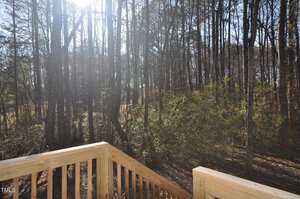 A deck with a wood railing and trees in the background.