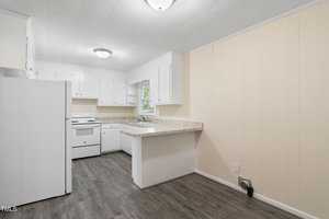 A small, empty kitchen featuring white cabinets, a white refrigerator, and a white stove. Light wood-patterned flooring contrasts with cream-colored walls. A single window above the sink provides natural light.