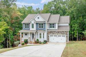 Nestled in Wake Forest, this charming two-story house at 1354 Red Bud Court boasts a gray and stone exterior with white trim. A front porch welcomes you, while a paved driveway guides you to the two-car garage. Surrounded by a lush grassy yard and dense trees, it's an idyllic retreat.