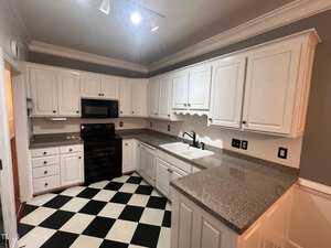 A kitchen with white cabinets and dark gray countertops. It features a black oven, stove, and microwave. The flooring is black and white checkerboard. The walls are a muted gray, and there's track lighting on the ceiling.