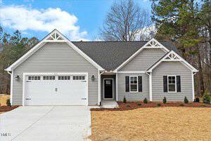 Located at 111 Averly Court, this charming single-story gray house with white trim and black shutters boasts a two-car garage and gable roof. The small front yard, nestled in the quaint town of Stem, features newly planted shrubs, framed by trees under a blue sky with scattered clouds.