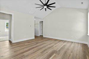 Empty room with light wood flooring and pale walls. A ceiling fan with a light is centered above. Two doorways lead to other areas, and a window on the right allows natural light. The room has a clean, modern appearance.