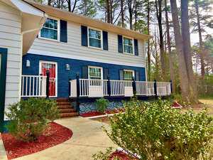 Situated at 1517 Peace Street in Henderson, this two-story house boasts a blue and white facade enveloped by trees. A striking red door and white railings greet you, while a walkway lined with shrubs and red mulch guides you to the welcoming steps.