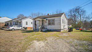 Located at 415 Cherry Street, this single-story, weathered white house in Oxford features a small porch with steps leading to the entrance. A concrete path and grassy yard sit out front, alongside a white car. On the right, two trash bins and children's play equipment are visible.