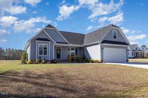 A single-story gray house on 560 Waterstone Lane in Henderson, with white trim and a gabled roof, features a charming front porch and a two-car garage. Set on a grassy lawn under partly cloudy skies, shrubs are neatly planted along the front.