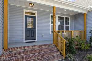 A house front entrance with blue-gray siding and a small covered porch. There is a dark blue door with a window and a row of brick steps leading up to it. The porch has wooden railings and posts. The number "560" is displayed on the wall.