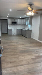 A spacious, empty kitchen and dining area with light wood flooring and gray cabinetry. The ceiling has recessed lighting and a fan with lights. A microwave is installed above the countertop, and there's a visible entrance to another room.