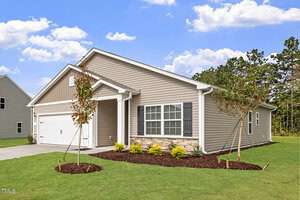 Located at 101 Shelfit Trail in Oxford, this charming single-story house features beige siding, a white garage door, and a quaint front porch. The yard boasts young trees and shrubs under a clear sky with a few clouds, set against a backdrop of mature trees.