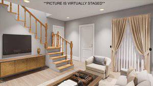 A modern living room with light gray walls and wood flooring. It includes a staircase with wooden railings, a flat-screen TV on a wooden console, a beige sofa and armchair, a coffee table, and curtains on a tall window. The image is virtually staged.