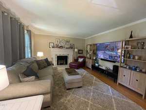 Living room with a large gray sectional sofa, an ottoman, and a red armchair. A wall-mounted TV is on the right, showing a building scene. The fireplace is centered with a mantel displaying decor, and bookshelves flank both sides.