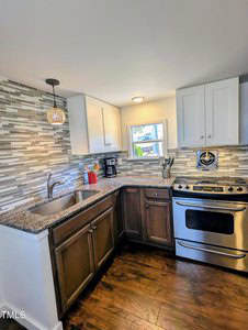 A modern kitchen with a stainless steel oven and stove, granite countertops, and a dual-basin sink. The backsplash features a multicolored tile design. There are upper and lower cabinets and a small window above the sink. A pendant light hangs overhead.