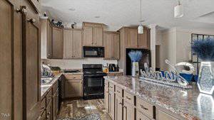 A kitchen with wooden cabinets, a marble-patterned countertop, and a dark electric oven. There are modern pendant lights, decorative vases with blue dried flowers, and a metallic "Welcome" sign on the counter.