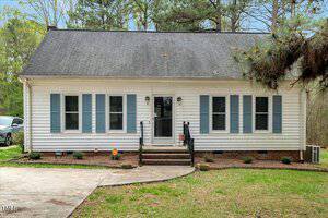 Nestled at 5578 Tabbs Creek Church Road, this charming single-story house boasts light blue shutters and a dark roof. Twin front doors open onto steps leading up, while trees gracefully frame the backdrop and a concrete driveway stretches out in the foreground.