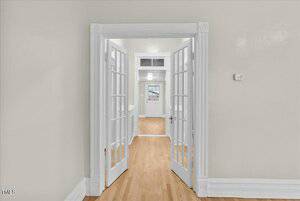 A hallway with light wooden floors and pale green walls features a series of open French doors aligned to show a receding view of rooms. White trim outlines the doors and ceiling. A white door is visible at the end of the passage.
