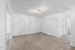 An empty room with light wood flooring and white walls. A ceiling light fixture is present, and there are doorways leading to other areas. The room has a minimalist and clean appearance.
