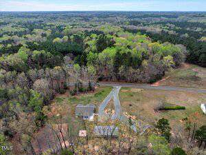 Aerial view of a rural landscape with a house surrounded by trees and open fields. A winding driveway leads to the house, and a railway track runs parallel to the property. Extensive wooded areas stretch into the distance.