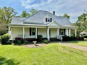 Nestled at 4715 Jacksontown Road in Manson, this white house features a gray roof and a charming covered front porch. The well-maintained yard boasts a lush lawn, a small garden, and a birdbath near the walkway, with trees and shrubs surrounding the property and a gazebo gracing the background.