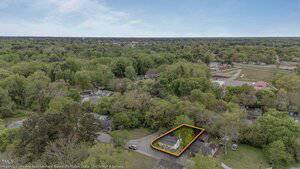 Aerial view of a residential neighborhood with many trees; one property near the bottom center is outlined in orange, highlighting a white house and yard.