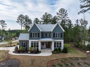 Located at 3908 Sage Court in Wake Forest, this two-story gray and white house features a covered front porch, attached garage, large lot with a curved driveway, minimal landscaping, and is surrounded by tall trees.