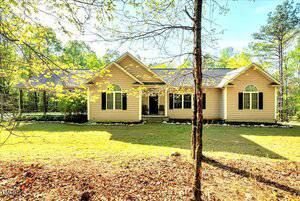 Charming single-story beige house at 452 Dogwood Trail in Henderson, featuring dark shutters, arched windows, a covered front entrance, and lush trees and grass with leaves scattered in the foreground.