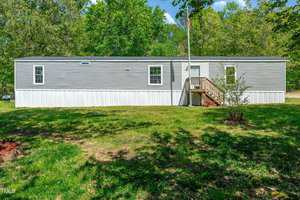 A single-wide gray and white manufactured home at 4045 Hillside Drive, Franklinton, featuring a small front porch and stairs, set on a grassy lawn surrounded by trees on a sunny day.