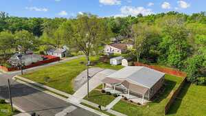 A single-story house with a covered porch sits on a corner lot at 212 Orange Street, Oxford. The large, neatly mowed lawn is surrounded by nearby houses and trees, while two storage sheds are visible in the backyard.