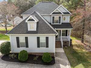 Charming two-story gray house on 2760 Clifton Avenue in Creedmoor, featuring black shutters, a gabled roof, brick accents, covered front porch, and a concrete walkway. Shrubs line the front and mature trees surround the property.