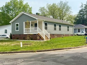 Charming single-story gray house with white trim and a brick foundation at 209 King Street, Oxford. Features a covered front porch with stairs on a corner lot bordered by grass, a small tree, street, and sidewalk.