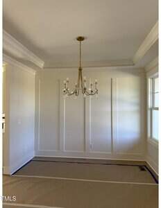 A mostly empty dining room with cream-colored walls, a coffered ceiling, and a gold chandelier. The floor is covered with protective brown paper, and there is a window on the right letting in natural light.