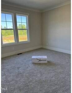 An empty carpeted room at 1403 Cottondale Lane in Wake Forest features beige walls, a white baseboard, double windows, and a single boxed ceiling fan sitting near the center of the floor.