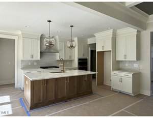Modern kitchen with white cabinets, a stainless steel stovetop and oven, a large central island with a wood finish and marble countertop, two globe pendant lights, and protective sheets covering the floor.