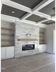 A modern living room with a coffered ceiling, built-in shelves and cabinets on either side of a fireplace with a tiled surround and a wooden mantel. The floor is covered with protective plastic sheeting.