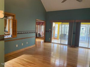 A spacious room with teal walls, light hardwood floors, a pass-through window to a kitchen, double doorways leading to a bright sunroom, and sliding glass doors opening to a screened porch.