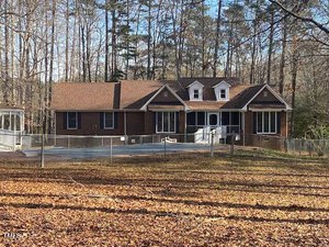 A single-story brick house at 80 White Deer Lane in Henderson features a brown roof, dormer windows, a fenced yard, and a screened porch, all surrounded by leafless trees and a yard covered in fallen leaves.