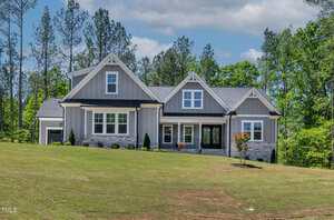 A modern, gray two-story house with white trim and a front porch sits on a large grassy lawn at 3925 Cedar Knolls Drive in Youngsville, surrounded by tall trees under a partly cloudy sky.